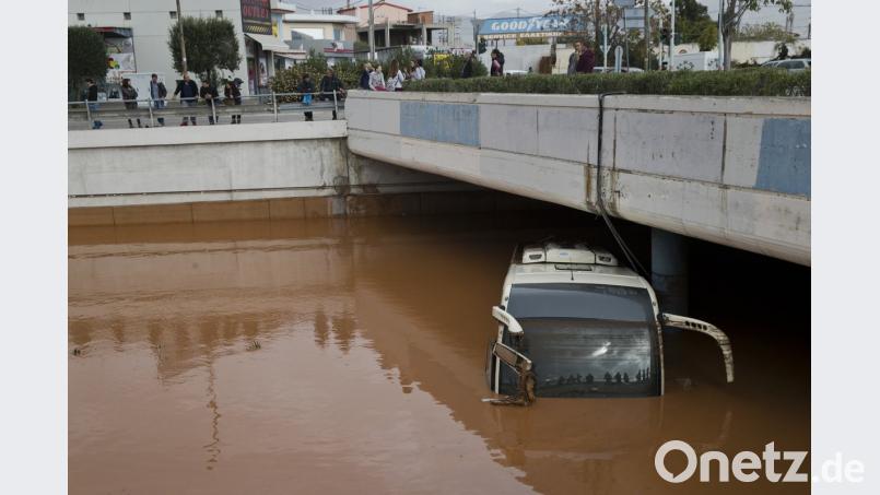 Mehrere Menschen spiegeln sich in der Frontscheibe eines Busses, der bis zum Dach im Wasser steht. Überschwemmungen haben in Griechenland mehrere Menschenleben gefordert.	Bild: Petros Giannakouris/AP/dpa