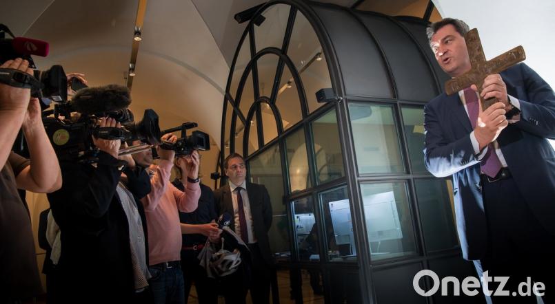 Markus Söder, Bayerischer Ministerpräsident (CSU), hält ein Kreuz, das er im Eingangsbereich der bayerischen Staatskanzlei aufhängt. Peter Kneffel/dpa