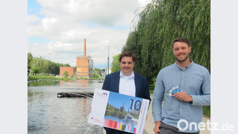 Zweimal Auenpark – einmal in der Realität und einmal auf der vierten Serie des MAKgutscheins. MAKnetisch-Vorsitzender Sebastian Macht und Innenstadt-koordinator Dominik Hartmann präsentieren das neue Motiv am Ort des Bildes. exb