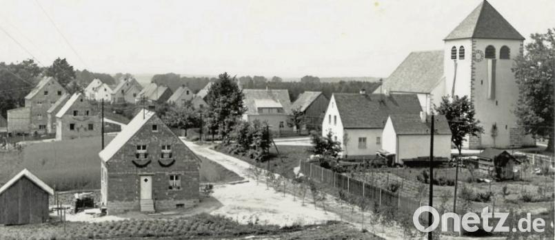Fronleichnam 1954:. Die Straße ist mit Birken geschmückt und mit Schilf bedeckt. Rechts ist der spätere Schulgarten zu sehen. Einige Parzellen sind noch unbebaut. Die Kirche wurde im August 1951 eingeweiht. Archivbild