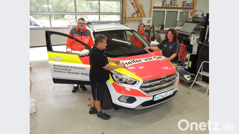 Stellvertretender Bereitschaftsleiter Patrick Hößl und HvO-Leiterin Jasmin Träger (in Einsatzkleidung) freuen sich über das neue Einsatzauto. Tanja und Bernd Hutzler bekleben in ihrer Firma das Auto. mor