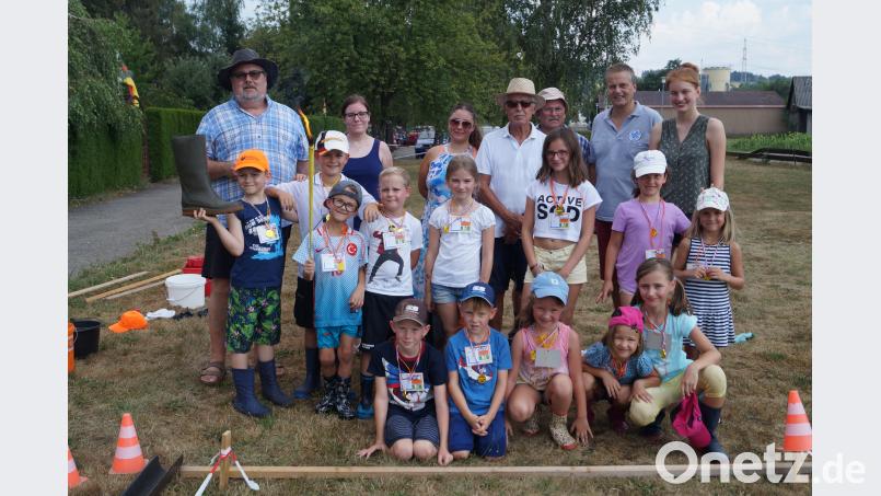 Trotz großer Hitze schaffen alle 12 Kinder die Anforderungen der "Gummistiefel-Olympiade" und freuen sich anschließend über Medaillen. Siedlerchef Walther Piehler (links, mit Schlapphut) und sein Team betreuen die Ferienaktion. du