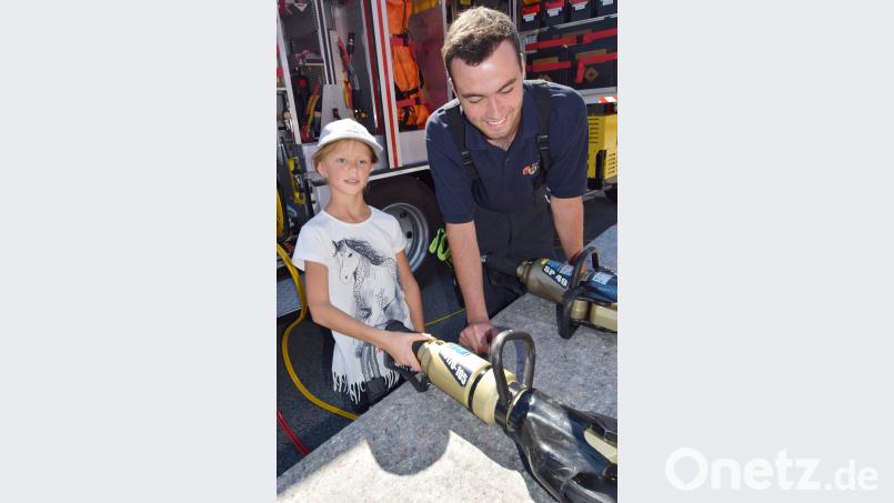 Ein Feuerwehranwärter erklärt dem Mädchen die Wirkungsweise einer Rettungsschere. no