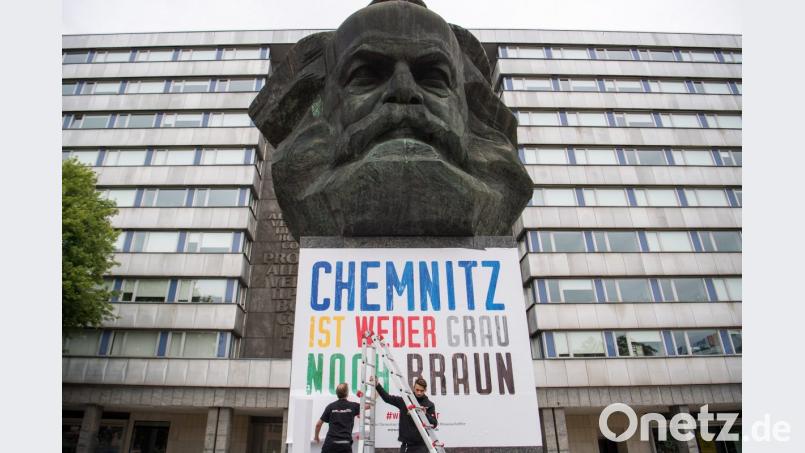 „Chemnitz ist weder grau noch braun“: Zwei Männer befestigen am Karl-Marx-Denkmal in Chemnitz ein Plakat. Bild: Monika Skolimowska