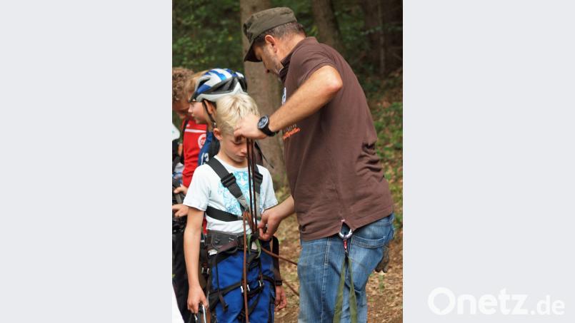 Heimatvereinsvorsitzende Hubert Haas legte den Kindern nach einer Einweisung die Klettergurte an. Bild: sön
