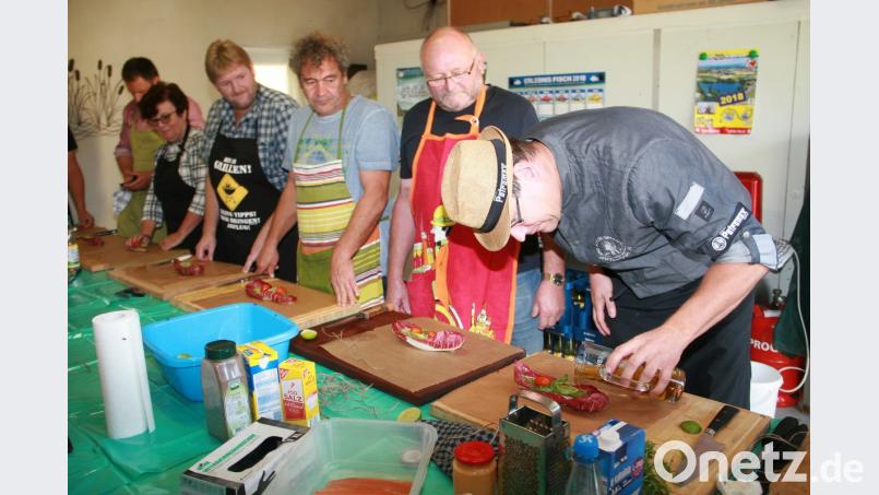 Karsten Heßing vom Freundeskreis der „Stiftlandgriller“ (rechts) macht es vor, wie das Olivenöl vorsichtig auf den vorbereiteten Saibling geträufelt werden muss. Bild: wro