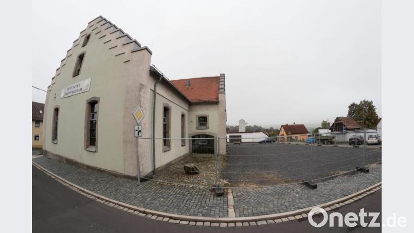 Auf diesem geschotterten Platz beim Knopfmuseum plant Architekt Georg Zunner ein Keller-Foyer, das von einem Erdhügel bedeckt ist. So entsteht eine kreative Lösung für den Notausgang und Rettungsweg im Obergeschoss (oberes Fenster), der dann über einen Steg auf den Hügel und den begrünten Vorplatz führt. Bild: dtr