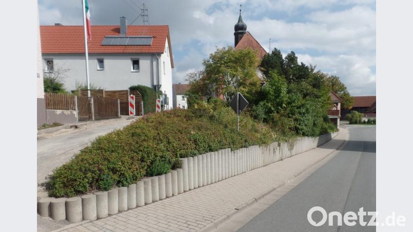 Die Betonpalisaden südlich der Sankt Anna Kirche (Mitte, im Hintergrund) sollen bei den Maßnahmen im Zuge der einfachen Dorferneuerung, vorbehaltlich einer Förderung, durch eine dorfgerechte Trockenmauer aus Granitsteinen ersetzt werden. Gleichzeitig soll das schadhafte Betonpflaster im Gehweg erneuert werden. Die dafür veranschlagten Kosten belaufen sich auf rund 54 000 Euro. Bild: Brendel, Hubert (BR)