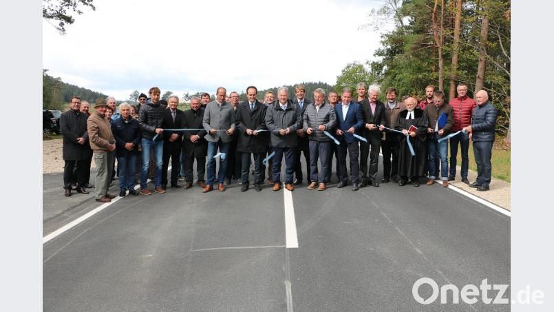 Landrat Richard Reisinger, die Bürgermeister Hans Koch und Hans-Jürgen Strehl (Bildmitte) durchtrennen gemeinsam mit den Bauverantwortlichen, den Grundeigentümern und etlichen Bürgern das Absperrband, um die neue Trasse offiziell zu eröffnen. Bild: gru