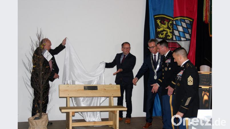Der ehemalige Leiter der VG-Geschäftsstelle, Robert Schön, und Partnerschaftsbeauftragter Martin Graser enthüllen eine Sitzbank, die an das Jubiläum erinnern soll. Sie ist ein Geschenk von Bürgermeister Werner, das unter anderem für Lieutenant Colonel John W. Copeland und Command Sergeant Major Joshua Kreitzer (von links) vom 709th Military Police Battalion bestimmt ist. Bild: stg