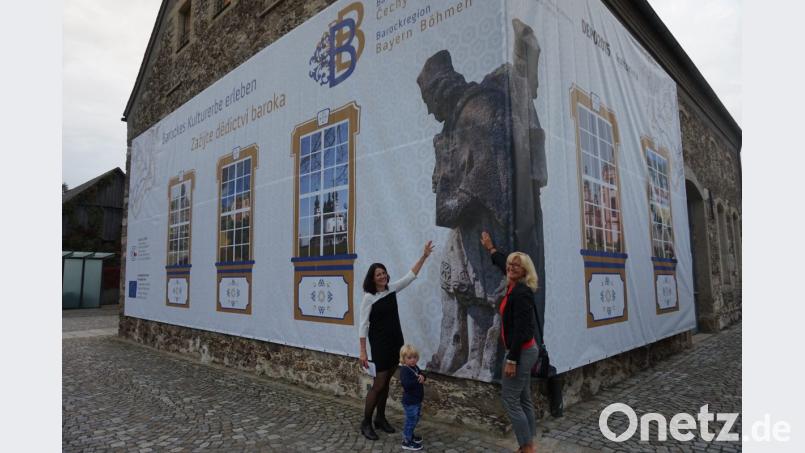 Bavaria Bohemia e.V. Vorsitzende Irene Träxler (rechts) und CeBB-Leiterin Veronika Hofinger mit Tochter Tylia (links) präsentieren das Banner zur Barockregion Bayern Böhmen an der Außenfassade des ehemaligen Kommunbräuhauses in Schönsee Bild: eib