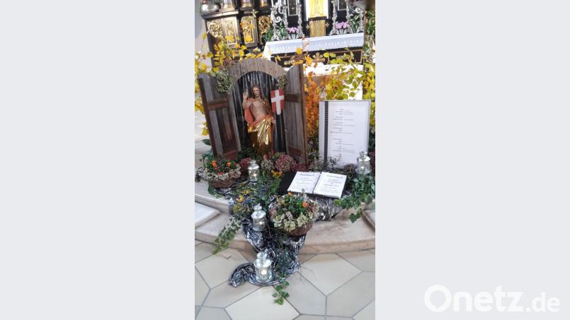 Vor dem Volksaltar liegt, herbstlich dekoriert, das Totenbuch der Pfarrei. Dahinter thront die Figur des auferstandenen Jesus, zugleich als Zeichen der Hoffnung. Bild: mng
