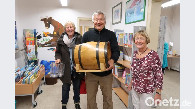 Autor Dieter Schraml (Mitte) weiß, was zu einem gelungenen Leseabend gehört. Für den gemütlichen Abend haben er und seine Frau Silvia (links) ein Fass Wein im Gepäck. Büchereileiterin Monika Seidel (rechts) freut sich riesig. Bild: bsc