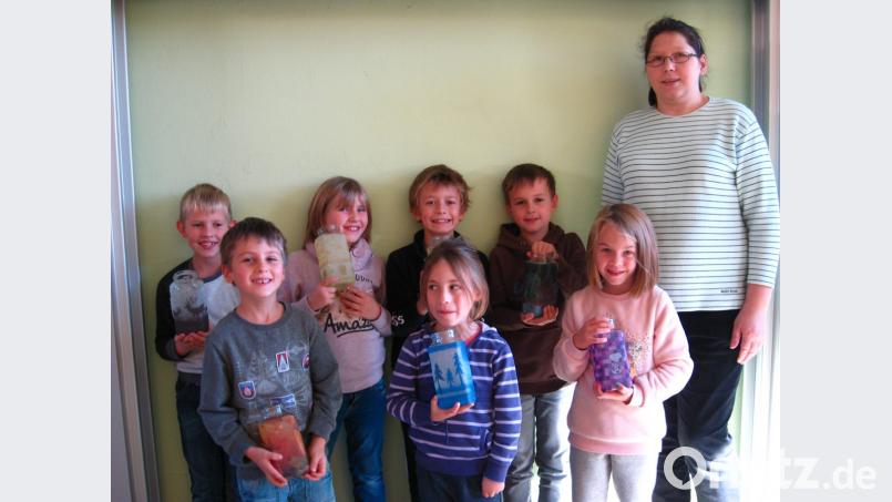 Leer Kaffeegläser erhalten hübsche Motive durch die Serviettentechnik. Die Kinder sind mit Betreuerin Silke Krämer stolz auf ihre schönen Windlichter. Bild: gi