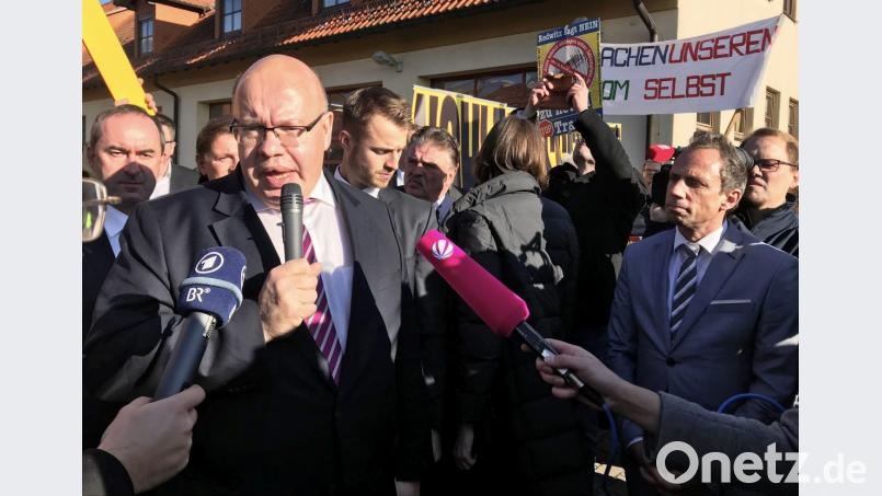 Peter Altmaier (CDU), Bundesminister für Wirtschaft und Energie, gibt In Redwitz ein Interview. Im Hintergrund demonstrieren Menschen gegen neue Stromtrassen. Bild: Wera Engelhardt/dpa