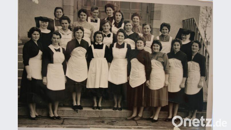 Erwartungsvoll und adrett in weißen Schürzen, ihrer „Dienstkleidung“, marschieren sie 1958 auf, die „Kocherln“, die Teilnehmerinnen an einem Koch- und Hauswirtschaftskurs im damaligen Elisabethenheim. Schwester Rodeberta (rechts) weiht sie in die Geheimnisse der Kochkunst ein, Schwester Edelhilde (links) gibt den jungen Damen Unterricht im Nähen. Bild: gpa