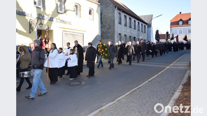 Ein langer Trauerzug macht sich nach dem Gedenkgottesdienst auf den Weg zum Kriegerdenkmal. Die Markträte Georg Stahl und Michael Troidl (von links) tragen den Kranz, den sie später am Ehrenmal niederlegen. Bild: fla