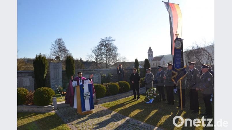 Pater Binu (am Pult) gedachte bei der Gedenkfeier am Ehrenmal im Unterauerbacher Friedhof der Gefallenen und Vermissten der Kriege. Die SKK Auerbachtal (rechts) hatte die Feier vorbereitet. Bild: ga