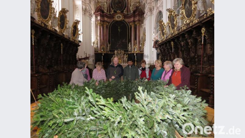 Mit vereinten Kräften und der Hilfe von Mesner Michael Burger und Kaplan John Gali haben die Frauen auch heuer wieder einen imposanten Adventskranz für die Basilika gebunden. Bild: ubb