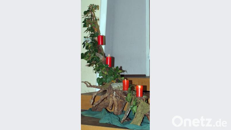 Eine große mit Efeu umrankte Wurzel, auf der drei der vier roten Adventskerzen flackern, schmückt die Bühne. Bild: Voigt, Ingrid