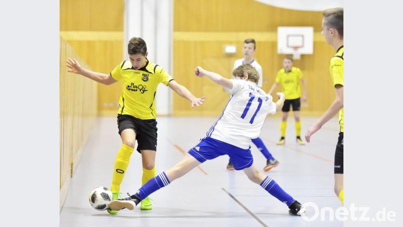 Mit dem Ball am Fuß läuft der Spieler des FC Amberg durch die Lücke zwischen Hallenwand und gestrecktem Bein des Gegenspielers vom TSV Großberg. Bild: Hubert Ziegler