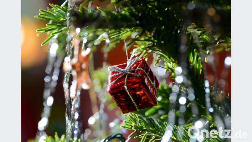 Ein kleines rotes Geschenkpaket als Weihnachtsbaumanhänger und Lametta hängen an einem Weihnachtsbaum. Bild: Jens Kalaene/dpa