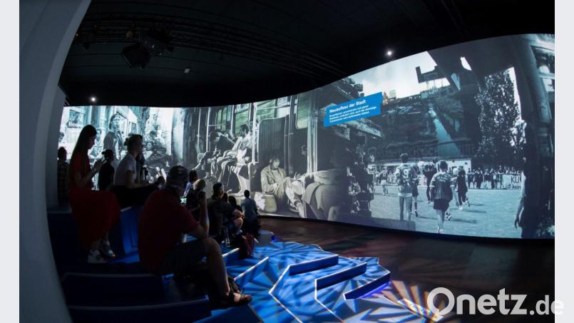 Besucher sitzen in der Alte Münze vor einer 270 Grad Leinwand. Dort können Besucher sich mit Bildern und Filmdokumenten über das Leben im ehemals geteilten Berlin informieren. Die Mediashow ist Bestandteil der Multimedia-Ausstellung "Nineties Berlin". Bild: Paul Zinken/dpa