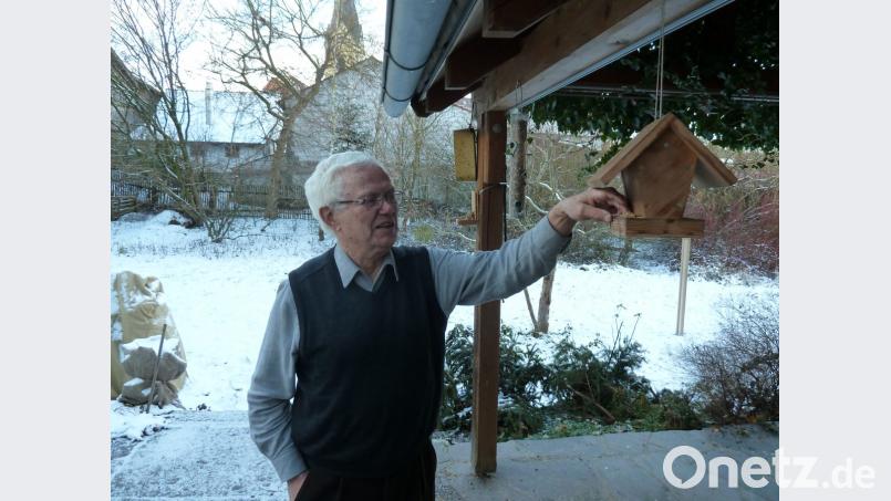 Professor Werner Schuler, Ehrenvorsitzender des LBV-Kreisverbands Schwandorf, hat auf der Terrasse (im Hintergrund die Niedermuracher Pfarrkirche) mehrere Futterstellen für Vögel angebracht. Bild: Portner