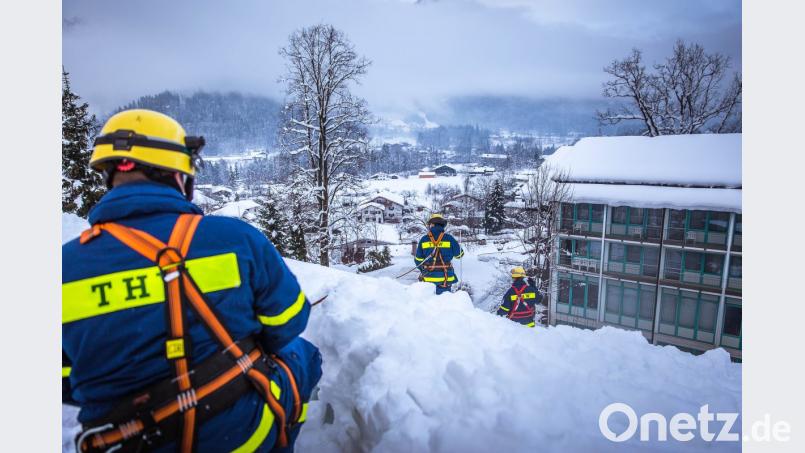 Meterhoch türmen sich die Schneeberge auf den Dächern. Mit Seilen sichern sich die Helfer. Bild: THW LV Bayern/Nicole Endres