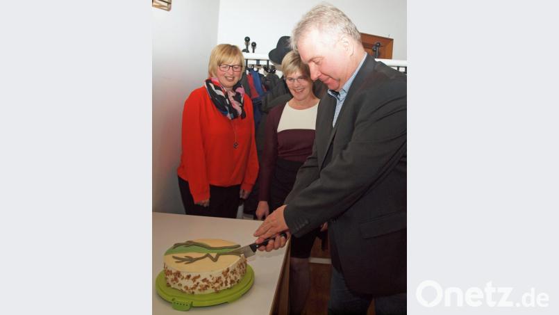 Markus Dollacker schneidet die mit Naturpark Hirschwald-Emblem verzierte Geburtstagstorte an. Claudia Straller und Barbara Hernes (von links), Projektleiterin Seniorenmosaik, hatten sie ihm überreicht. Bild: sön