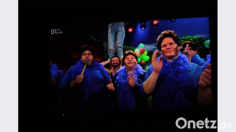 Im blauen Kleid mit Federboa ehren die Künstler, darunter Peter Fuhrmann und Lucky Schieder (von rechts) von der Altneihauser Feierwehrkapell&#039;n, beim Finale in Veitshöchheim die &quot;Mutter des Frankenfaschings&quot; Barbara Stamm. Anschließend feiern sie mit ihr bis zum Frühstück weiter. Screenshot: ui/Quelle: BR