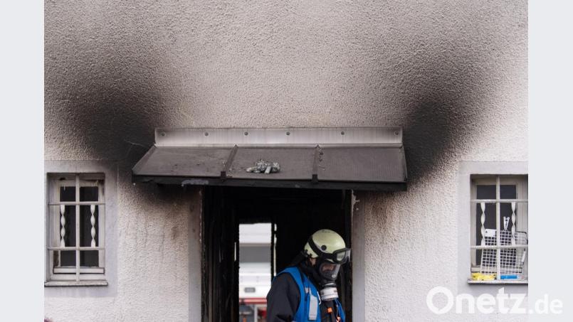 Ein Feuerwehrmann verlässt nach einem Brand ein Haus. Auf dem Dach über dem Eingang liegt ein angeschmortes Stofftier. Bild: Lino Mirgeler