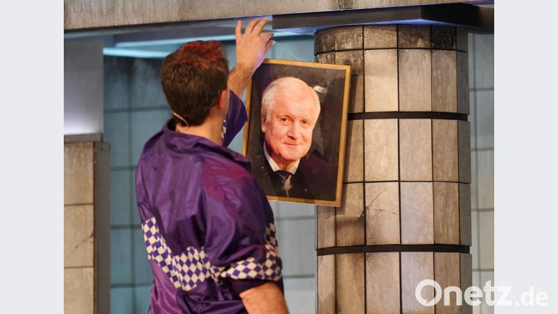 Stephan Zinner als Ministerpräsident Markus Söder hängt im Singspiel ein Bild von Horst Seehofer ab. Nach der Show kritisierte der echte Söder, dass sein Vorgänger als verwirrter Mann dargestellt wurde. Bild: Tobias Hase/dpa