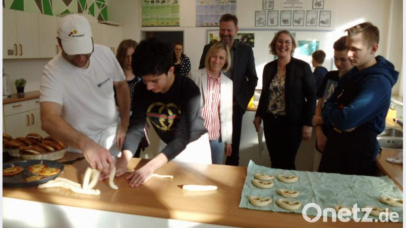 In der Schulküche demonstriert Marco Ries (links), Inhaber der örtlichen Bäckerei, wie man den Teig zur Brezen formt. Außer den Schülern beobachten ihn dabei Rektorin Gabriele Krettner, Bürgermeister Alwin Märkl und Konrektorin Andrea Widder. Bild: u