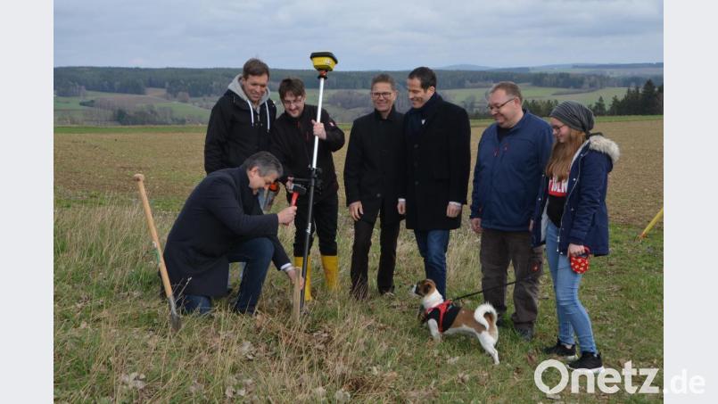 Bürgermeister Andreas Wutzlhofer (kniend) schlägt einen Pflock als Zeichen des Baubeginns ein. Ortssprecher Heimo Bauer und seine Tochter verfolgen die Zeremonie mit Bundestagsabgeordnetem Albert Rupprecht, Christian Schilling vom Netzbetreiber sowie den Vermessungstechnikern (von rechts). Bild: dob