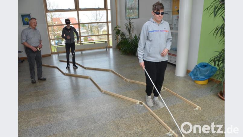 Nur mit einem Blindenstock erfühlen die Realschüler den vorgegebenen Weg. Noch schwieriger ist das anschließende Treppensteigen. Robert Götz (links) leitet die Schüler an. Bild: dob