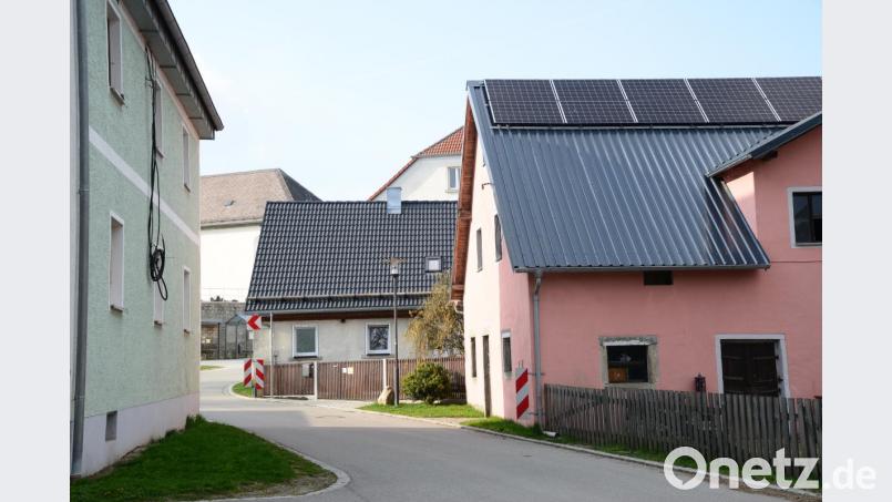 Die Straße zwischen dem grünen Haus (links) und dem rosafarbenen Haus (rechts) möchte der Eigentümer der Anwesen aufschneiden, um Versorgungsleitungen zu verlegen. Die bisherigen Stromleitungen verbanden die Häuser in luftiger Höhe. Ein landwirtschaftliches Fahrzeug mit unzulässiger Höhe hatte die Leitungen abgerissen, die jetzt am grünen Haus (links) lose herunterhängen. Bild: bey