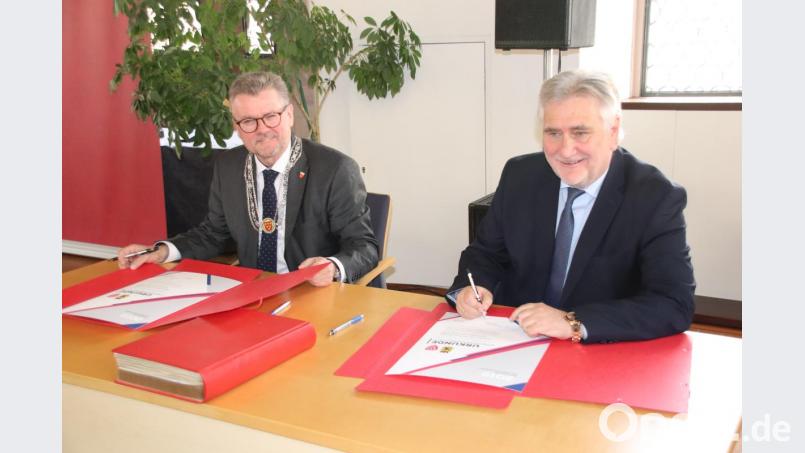 Die beiden Bürgermeister Michael Göth und Rudi Bertram (von links) unterzeichnen die Partnerschaftsurkunde. Bild: cog