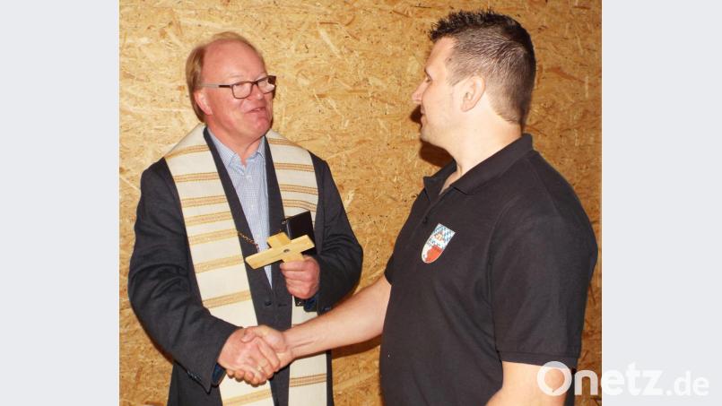 Pfarrer Wolfgang Bauer übergibt ein Holzkreuz an Florian Fischer (rechts). Bild: e