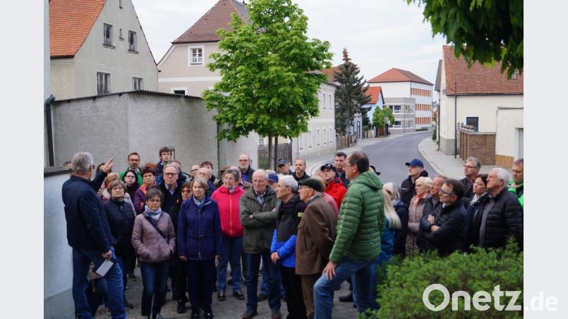Altbürgermeister Karl Balk (links) erklärt den fast 60 Bürgern beim historischen Spaziergang durch Schirmitz unter anderem auch die Geschichte von St. Jakob, dem alten Schulhaus (Mitte, links) und dem neuen Schul- gebäude (hinten, links). Bild: du