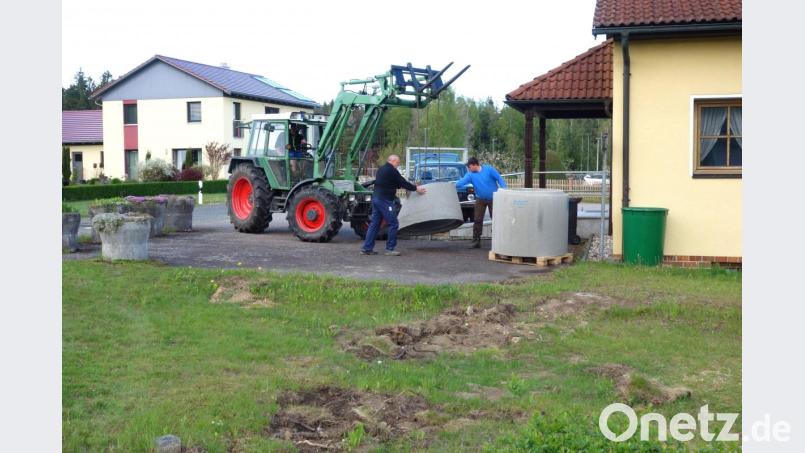 Durch die Unterstützung von Hubert Wildenauer (rechts) und Fabian Forster (im Traktor) ging die Anlieferung der Beton-Fertigteile für Hauptinitiator Ewald Zetzl reibungslos über die Bühne. Auf der Rasenfläche davor zeugen Erdarbeiten bereits vom künftigen Standort des neuen Dorfbrunnens. Bild: fjo