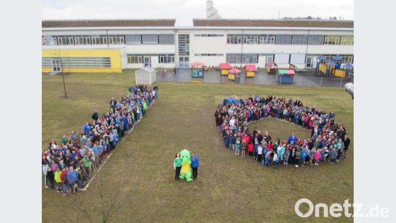 Die Netzaberg Elementary School feiert zehnjähriges Bestehen. Dafür formieren sich Schüler und Lehrkräfte zu einer Zehn. Mit dabei sind Rektorin Vanessa Färber (Mitte, von links), das Schulmaskottchen &quot;Netzi the Dragon&quot; und Konrektorin Sonya Gates. Bild: rn
