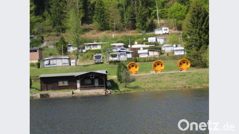 Blick vom anderen Seeufer aus auf einen Teil des Campingplatzes mit den drei Fässern. Platz ist in jedem Wohnfass für vier Personen, allerdings dann mit eng begrenztem Wohnraum. Bild: ubb