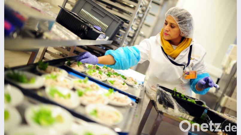 Eine Mitarbeiterin dekoriert Mahlzeiten in der Produktion der LGS Sky Chefs. Bild: Daniel Reinhardt/dpa