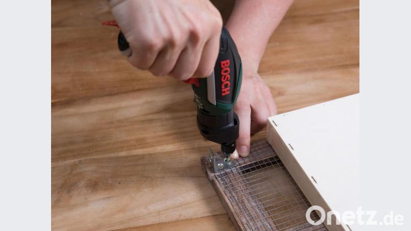 Metallwinkel werden in den Rahmenecken über dem Draht verschraubt, um Rückwand und Fenster zu fixieren. Bild: DYA/Bosch