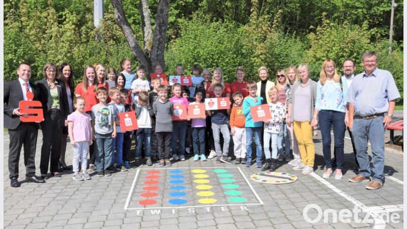 Bürgermeister Peter Braun (rechts) freut sich mit Sparkassenleiter Markus Hummel (links), den Lehrkräften, Kindern und Vertretern des Elternbeirates über die bunten Gesellschaftsspiele mitten im Verkehrsübungsgarten: Im Rahmen des „Jumi“-Förderprogramms der Sparkasse wurde der Pausenhof der Erasmus-Grasser-Grundschule verschönert. Bild: bö