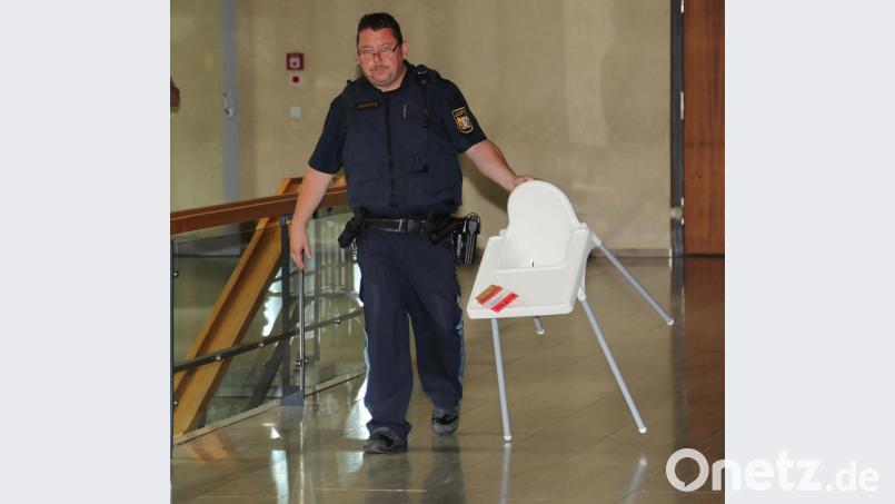 Ein Justizwachtmeister bringt den Kinderstuhl, auf dem die Tasse mit heißen Tee stand, mit dem sich das Kind verbrühte - wenn man die Variante der Mutter glaubt. Bild: ca