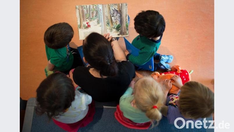 Eine pädagogische Fachkraft liest in einer Kindertagesstätte Mädchen und Buben aus einem Buch vor. In manchen Fällen empfiehlt es sich, Kinder von hinten und nicht identifizierbar zu fotografieren. Rückenansichten sind nicht schön, aber taugen zumindest als Notlösung. Symbolbild: Arno Burgi/ZB/dpa