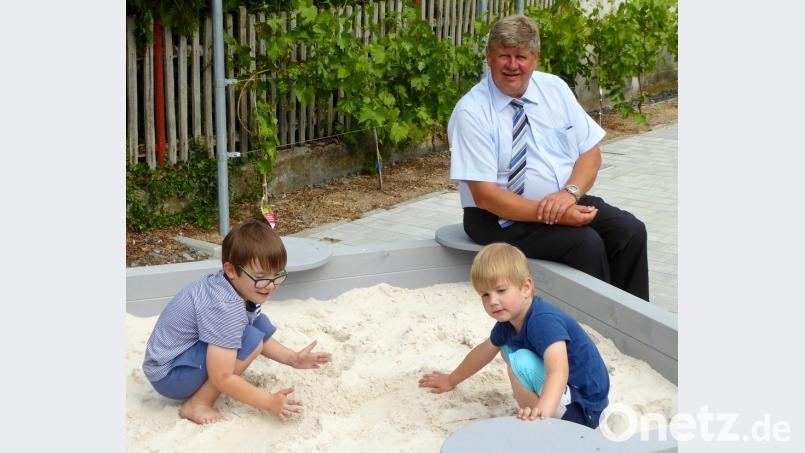 Die beiden Brüder Elias und Jonas freuen sich mit Bürgermeister Martin Schregelmann über den neuen Sandkasten auf dem Dorfplatz. Im Hintergrund ein Teil der von der Patengemeinde Algund spendierten Weinstöcke. Bild: fsb