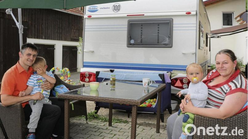 Tobias und Nicole Röttcher sitzen mit den beiden Kindern in ihrem neuen „Wohnzimmer“: Seit März leben sie in einem Wohnwagen vor dem Haus, das sie nicht mehr betreten dürfen. Bild: Wolfgang Steinbacher